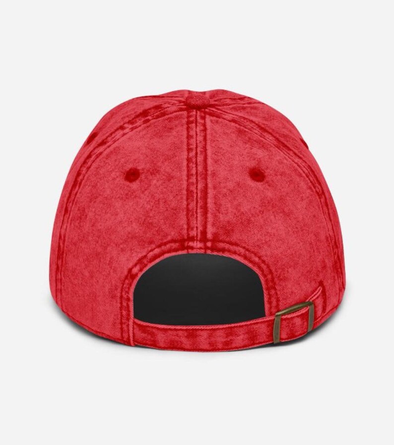 May include: A red baseball cap with a curved brim and a metal buckle closure. The cap has a vintage, worn look and a solid color design. The back of the cap is visible.