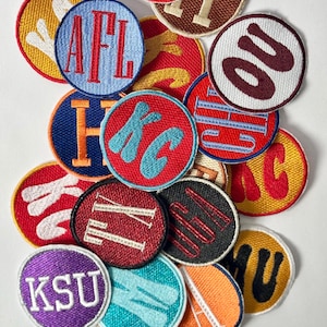 Op de afbeelding: Een verzameling kleurrijke geborduurde patches met verschillende letters en woorden, waaronder "AFL", "KC", "KSU" en "OU".