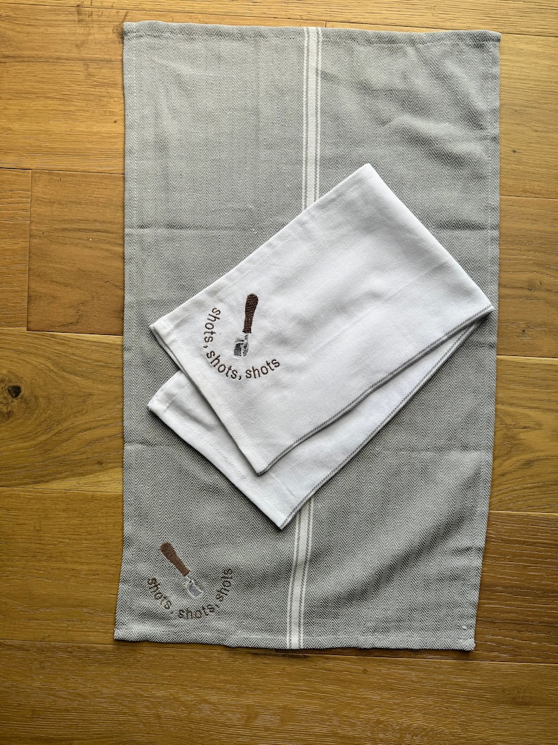 May include: Two gray and white striped kitchen towels with embroidered espresso machine and the text "shots, shots, shots".