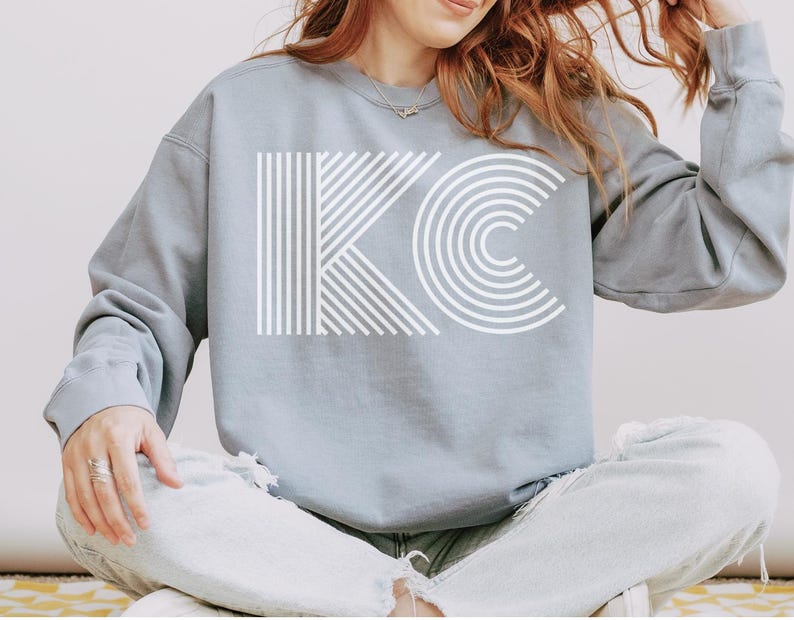 Pu&ograve; includere: Una felpa blu chiaro con le lettere bianche "KC" in un design geometrico audace. La "K" &egrave; composta da linee verticali e diagonali, mentre la "C" &egrave; formata da semicerchi concentrici. La felpa &egrave; uno stile casual e confortevole.