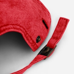 May include: Close-up of a red baseball cap with a curved brim. The cap features a metal clasp and a fabric strap for adjustment. The cap is made of a textured fabric.