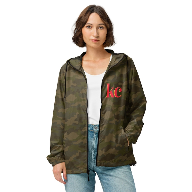 Brunette woman wearing Camo Kansas City unisex lightweight zip up windbreaker with printed KC on left chest pocket.