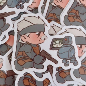 May include: A stack of stickers featuring a cartoon character wearing a grey and brown outfit and a black eye patch. The character is holding a gun and standing next to a small robot.