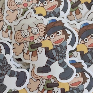 K&ouml;nnte beinhalten: Eine Sammlung von Cartoon-Aufklebern. Einer zeigt eine affen&auml;hnliche Figur mit Brille und Laborkittel, die eine Waffe h&auml;lt. Der andere zeigt einen Soldaten in einer blau-grauen Uniform, ebenfalls mit einer Waffe. Die Aufkleber haben einen wei&szlig;en Rand.
