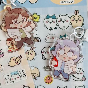 May include: Two clear acrylic charms featuring cartoon characters with glasses and white lab coats. The characters are holding a clipboard and a bottle of ketchup. The charms are surrounded by smaller stickers of cartoon animals and objects. The text on the packaging reads "ウリ デー ル ちい が お ③ シャンプ".