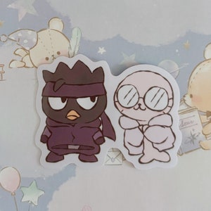 May include: Two cartoon stickers, one of a purple ninja with a black mask and the other of a pink seal wearing glasses and a white coat.