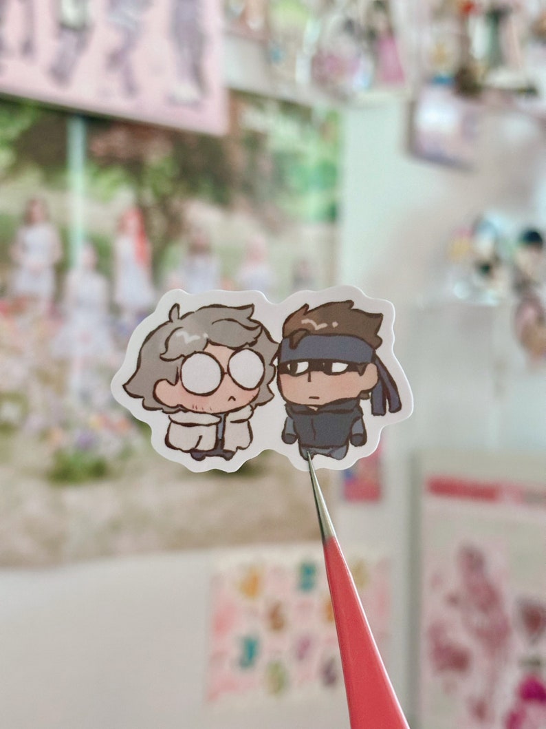 May include: Two cartoon characters, one with gray hair and glasses wearing a white coat and the other with brown hair wearing a blue jacket and a headband, are depicted on a white sticker.
