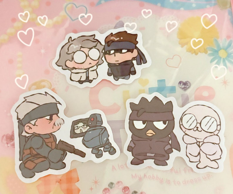May include: A set of five cartoon character stickers featuring a man with a white beard, a man with a black eye mask, a man with a gray eye mask, a robot, and a man with glasses. The stickers are on a pink background with white hearts.