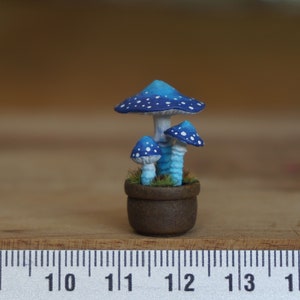 Può includere: Un vaso da fiori in miniatura a forma di fungo blu e bianco con tre funghi. Il vaso è marrone e ha una texture ruvida. I funghi sono dipinti con punti bianchi.