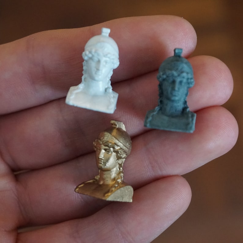 May include: Three small busts of a woman wearing a helmet, one is white, one is gray, and one is gold.