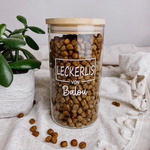 Könnte beinhalten: Ein klares Glasgefäß mit Bambusdeckel gefüllt mit braunen Hunde-Leckerlis. Das Gefäß hat ein weißes Etikett mit der Aufschrift "Leckerlis von Balou".