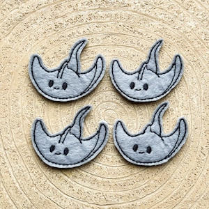 Peut inclure: Quatre patchs en feutre gris en forme de raies avec des yeux brodés et des bouches souriantes.