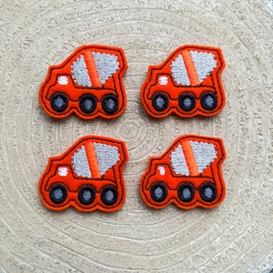 May include: Four orange felt cement mixer trucks with black wheels and white stripes. The trucks are embroidered with white stitching.