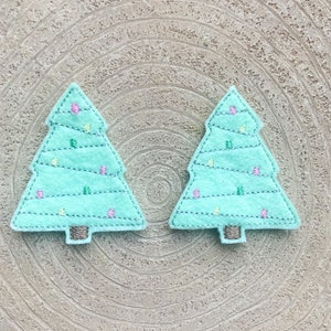 Peut inclure: Deux sapins de Noël en feutre avec des lumières vertes et blanches et des ornements roses. Les sapins sont sur un fond brun clair.