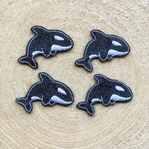 May include: Four black felt or fabric orca whale appliques with white accents. The orcas are in a circular pattern on a light brown wood background.