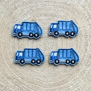 May include: Four blue felt applique garbage trucks on a wood background. The trucks are all facing the same direction and have a simple design.