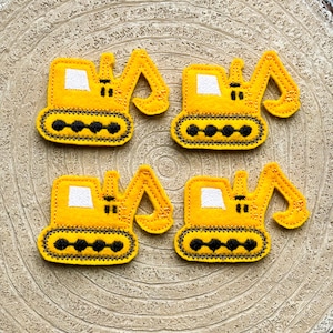 Könnte beinhalten: Vier gelbe Filz-Applikationen eines Baggers mit schwarzen und weißen Details. Die Applikationen befinden sich auf einem Holzgrund.
