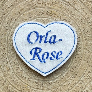 Può includere: Toppa a forma di cuore bianca con testo ricamato in blu che recita "Orla-Rose".