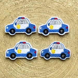 以下が含まれることがあります： 黄色い星のディテールが付いた、青と白のフェルト製の警察の車のワッペンが4つ。ワッペンは金色の背景の上にあります。