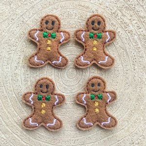 May include: Four felt gingerbread man decorations with white icing details, green bow ties, and gold buttons.