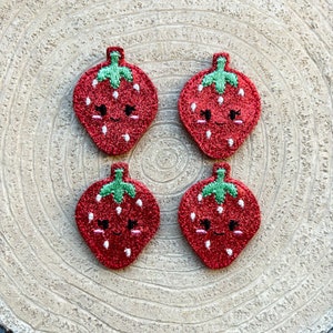 Peut inclure: Quatre patchs de fraises rouges pailletées avec des feuilles vertes et des visages souriants brodés en blanc.
