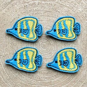 May include: Four blue and yellow embroidered felt fish with a striped pattern. The fish are arranged in a square pattern on a light brown wooden surface.