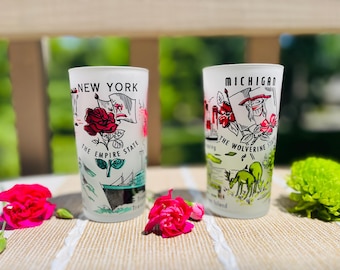 May include: Two frosted glass tumblers featuring state-themed illustrations. The left glass displays 'NEW YORK THE EMPIRE STATE' with a red rose and ship. The right glass displays 'MICHIGAN THE WOLVERINE STATE' with a deer and floral graphics.
