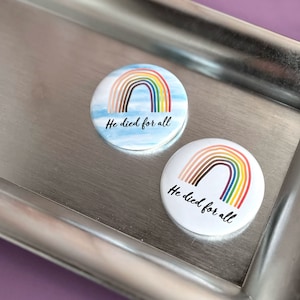 May include: Two round white buttons with a rainbow and the text "He died for all".