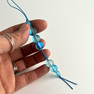 May include: A blue and white beaded phone charm with a knotted cord.