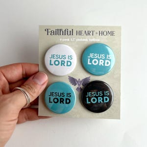 May include: Four 1.5 inch pinback buttons with the text "Jesus is Lord" in white lettering on a teal background. Two buttons have a white background and two buttons have a black background.