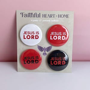 May include: Four 1.5 inch pinback buttons with the text "Jesus is Lord" in red and black lettering on white, red, and black backgrounds. The buttons are arranged in a square on a white card with the text "Faithful Heart + Home" and "4 pack 1.5" pinback buttons" printed on it.