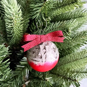 May include: A red and white Christmas ornament with a pink glitter bow. The ornament is filled with white paper scraps and has a red and white glitter finish.