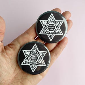 May include: Two black and white round buttons with a six-pointed star design. The text "Never Again Is Now" is repeated around the star.