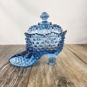 May include: A blue glass shoe-shaped candy dish with a lid. The dish is covered in small raised dots.