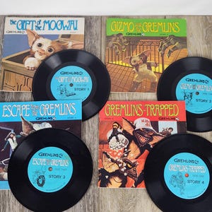 May include: A collection of vintage Gremlins story records and accompanying illustrated covers. The records are black with light blue labels. The covers feature colorful illustrations of characters and scenes from the movie.