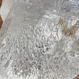 May include: A large, clear, raw quartz crystal specimen with a jagged, multifaceted surface. The stone features natural internal fractures and inclusions, with a transparent, glass-like appearance and sharp, irregular edges throughout its structure.