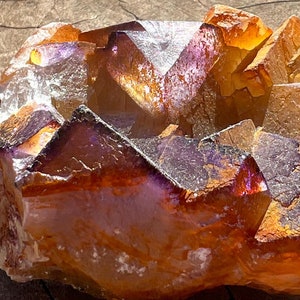 May include: A large, orange and purple amethyst crystal cluster with a rough, natural texture. The crystal is illuminated by sunlight, highlighting its facets and translucence.