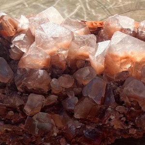 May include: A cluster of reddish-brown calcite crystals with a rough, natural texture. The crystals are translucent and have a slight pink hue. The cluster is about 6 inches long and 3 inches wide.