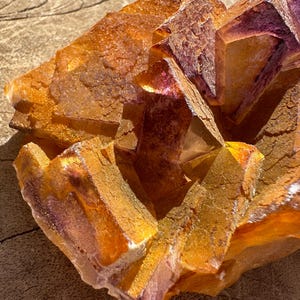 May include: A cluster of orange and purple fluorite crystals with a rough, textured surface. The crystals are arranged in a geometric pattern, creating a visually appealing and unique piece.