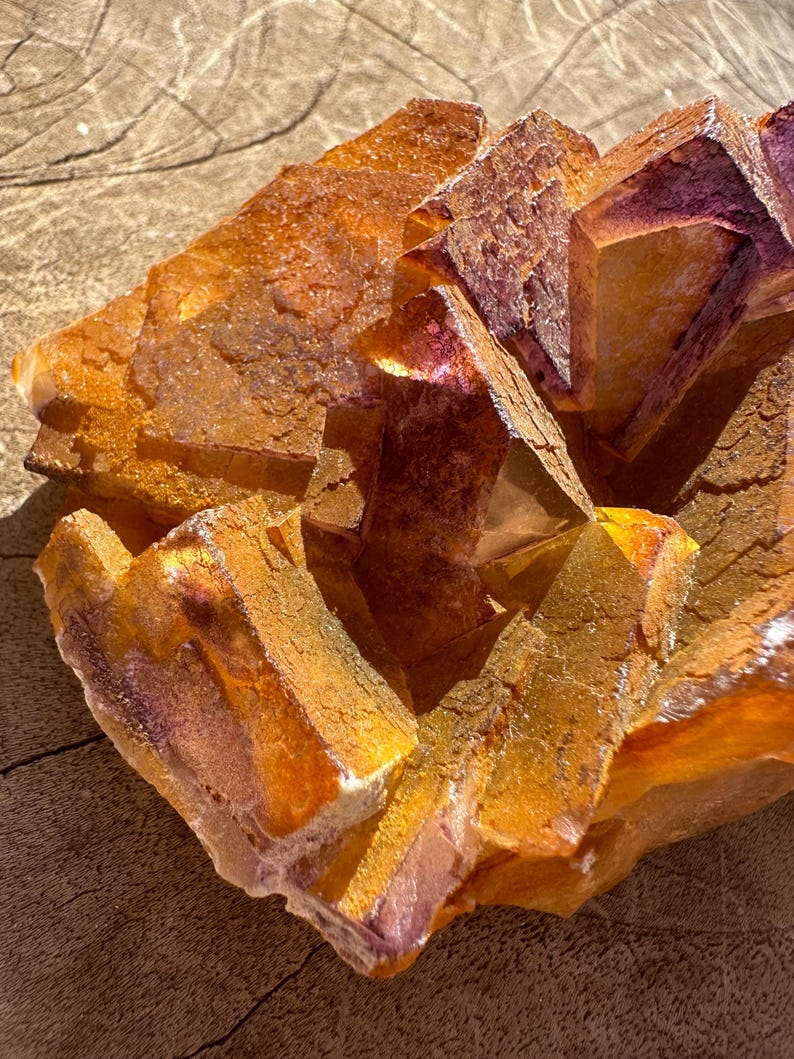May include: A cluster of orange and purple fluorite crystals with a rough, textured surface. The crystals are arranged in a geometric pattern, creating a visually appealing and unique piece.