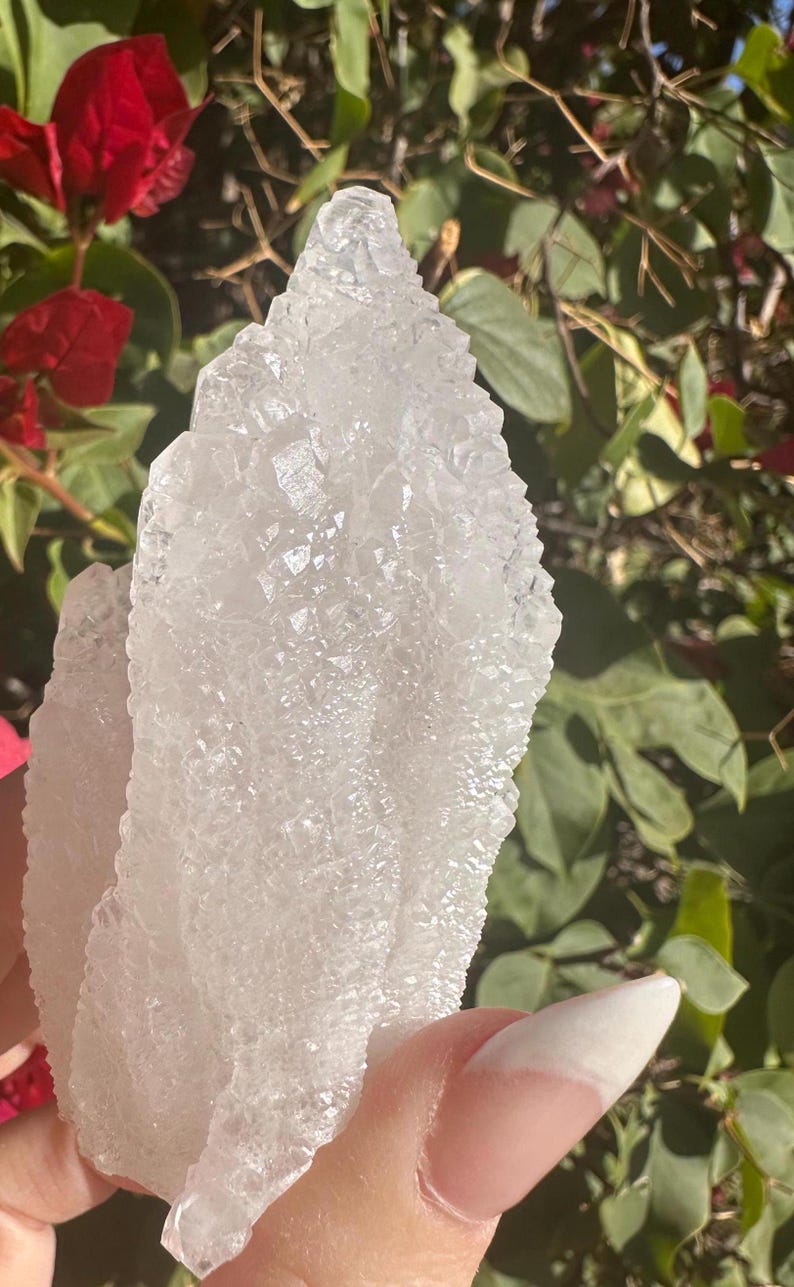 Puede incluir: Un gran c&uacute;mulo de cristales blancos transparentes con una superficie rugosa y texturizada. El cristal tiene forma de abanico o de hoja.