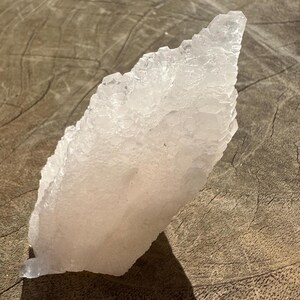 Puede incluir: Un gran c&uacute;mulo de selenita cristalina blanca con un delicado tono rosado. La selenita est&aacute; dispuesta en una formaci&oacute;n puntiaguda en forma de abanico.