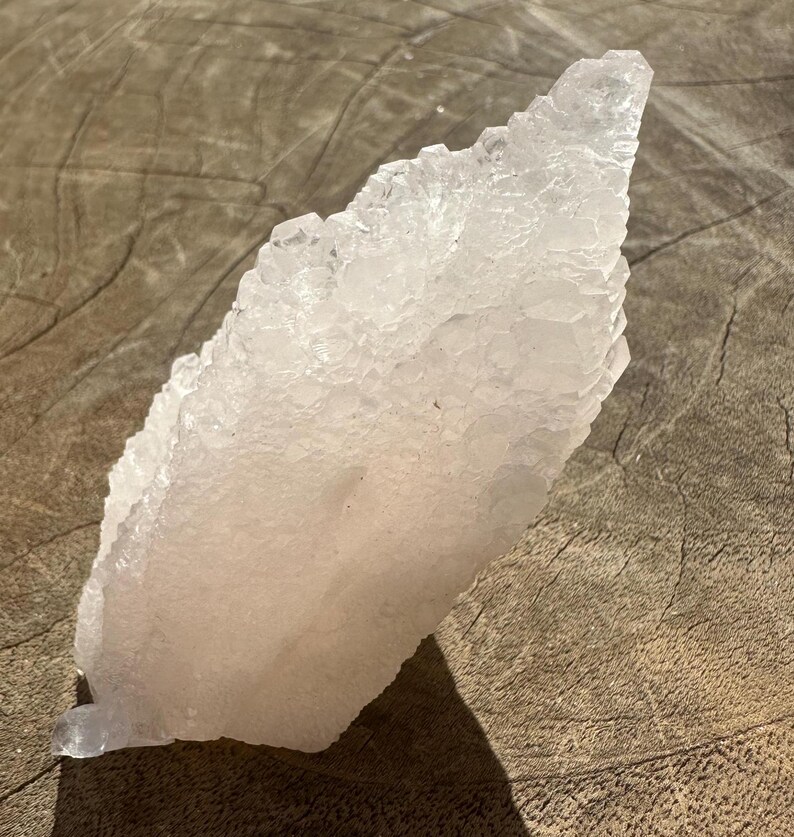 Puede incluir: Un gran c&uacute;mulo de selenita cristalina blanca con un delicado tono rosado. La selenita est&aacute; dispuesta en una formaci&oacute;n puntiaguda en forma de abanico.