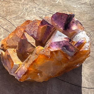 May include: A large cluster of amethyst crystals with a purple and orange color. The crystals are arranged in a cluster and have a rough, natural texture.
