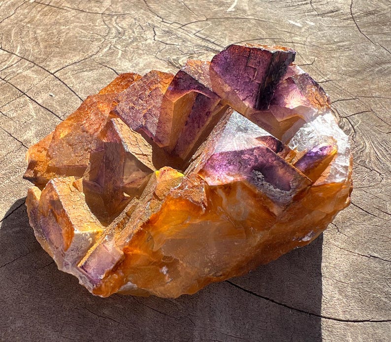 May include: A large cluster of amethyst crystals with a purple and orange color. The crystals are arranged in a cluster and have a rough, natural texture.
