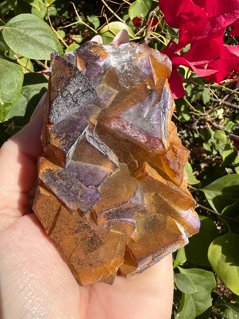 May include: A large, natural, purple and orange fluorite crystal cluster. The crystal has a rough, textured surface and is a beautiful example of this mineral.