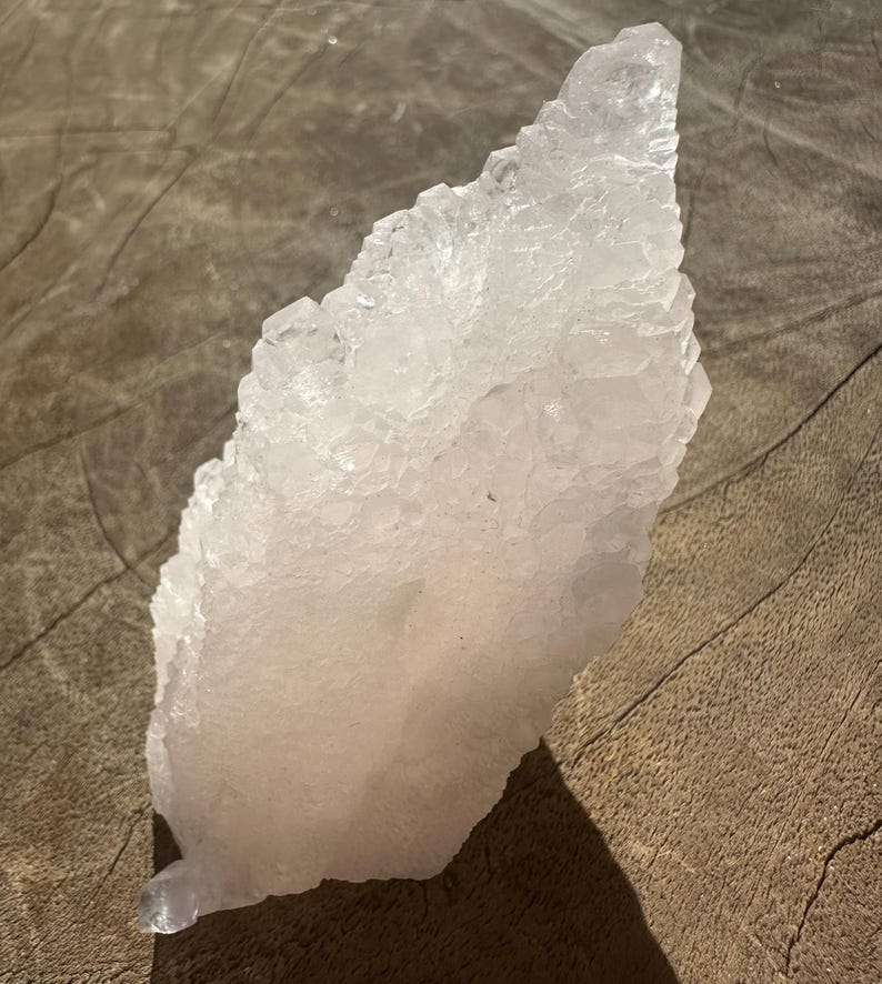 Puede incluir: Un gran c&uacute;mulo de cristales rosa con una punta puntiaguda. El cristal es transl&uacute;cido y tiene una superficie rugosa y texturizada.