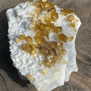 May include: A natural mineral specimen featuring a white, crystalline base with clusters of golden-yellow crystals. The crystals have a sparkling, translucent appearance. The overall shape is irregular, showcasing the raw beauty of the stone.