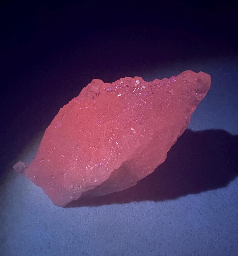 Puede incluir: Una roca grande, rosada y cristalina con una superficie rugosa y texturizada. La roca est&aacute; iluminada desde un lado, proyectando una sombra sobre la superficie de abajo.