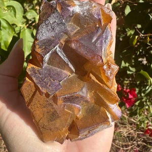 May include: A large, multi-faceted crystal cluster with a mix of purple and orange hues. The crystal has a rough, natural texture and is a beautiful example of a fluorite specimen.